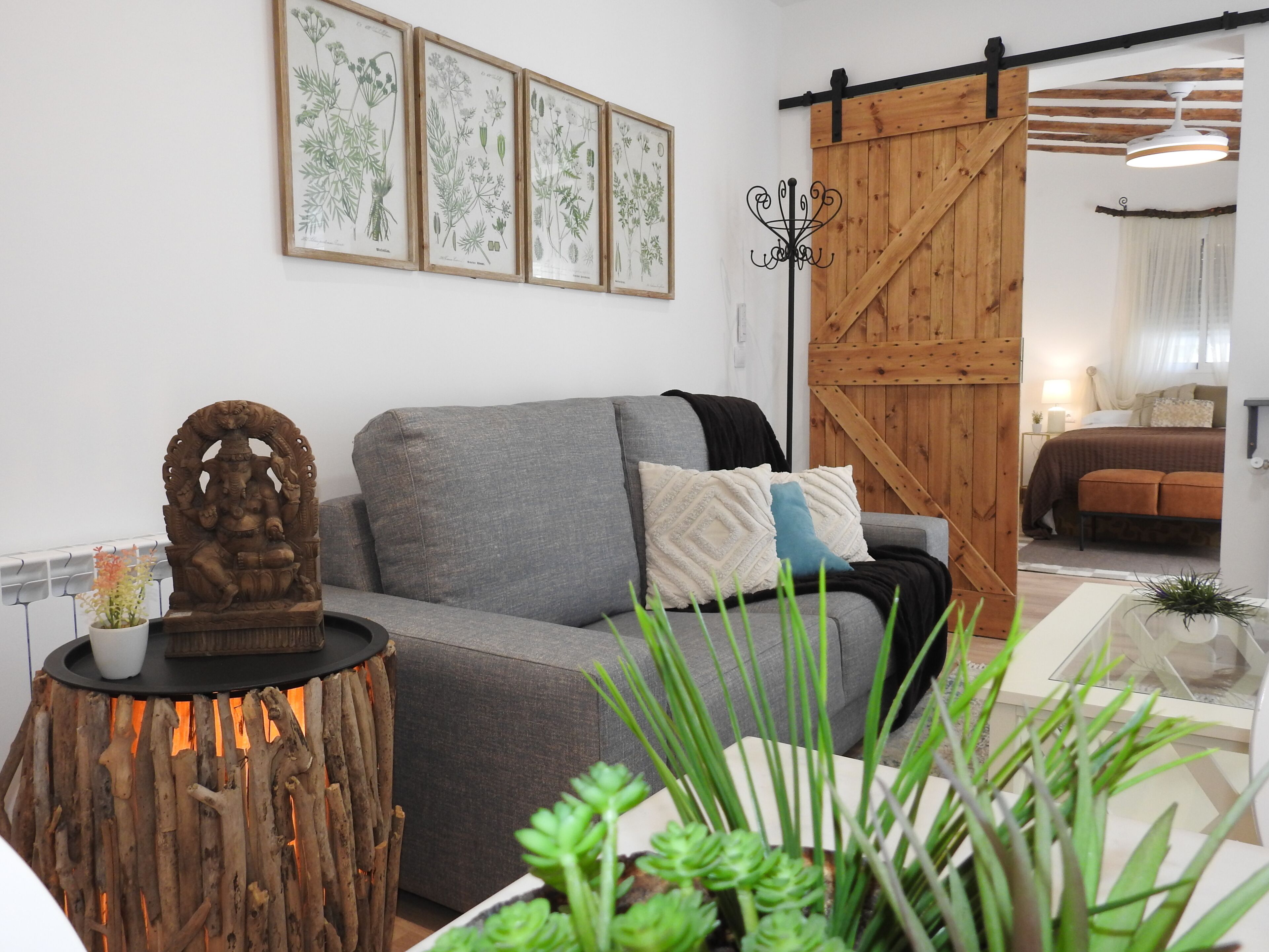 A living room with a grey sofa, a wooden sculpture, and framed botanical illustrations on the wall.