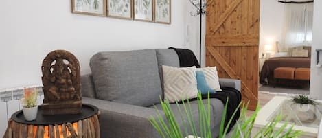 A living room with a grey sofa, a wooden sculpture, and framed botanical illustrations on the wall.