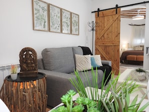 Un salón con un sofá gris, una escultura de madera e ilustraciones botánicas enmarcadas en la pared.