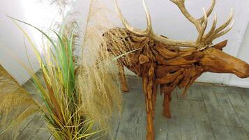 Una escultura de cabeza de venado de madera con astas, una planta en maceta con hierbas altas, y una pared lisa.