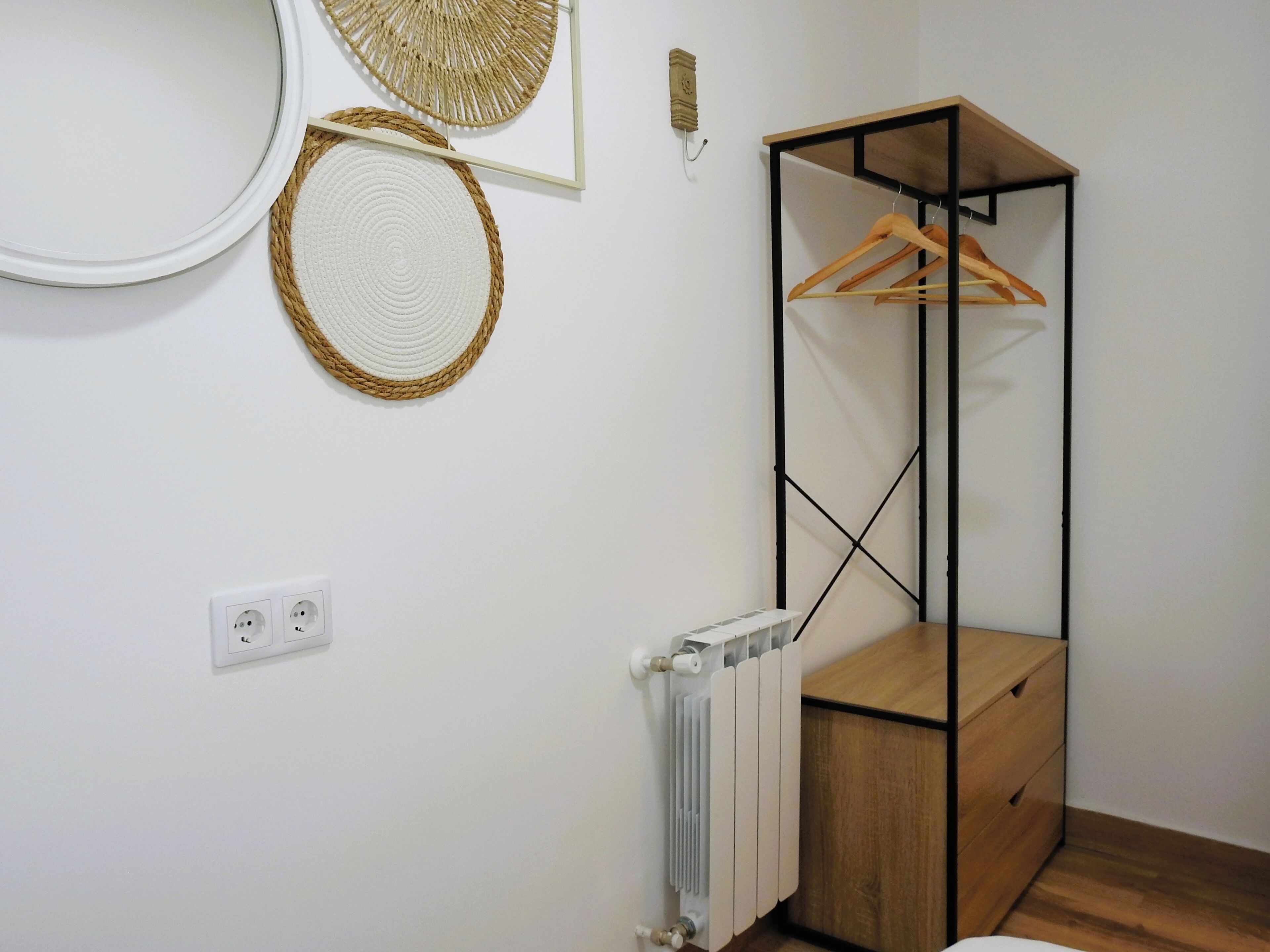 A room with a radiator, a wooden cabinet, and a metal shelving unit with wooden hangers.