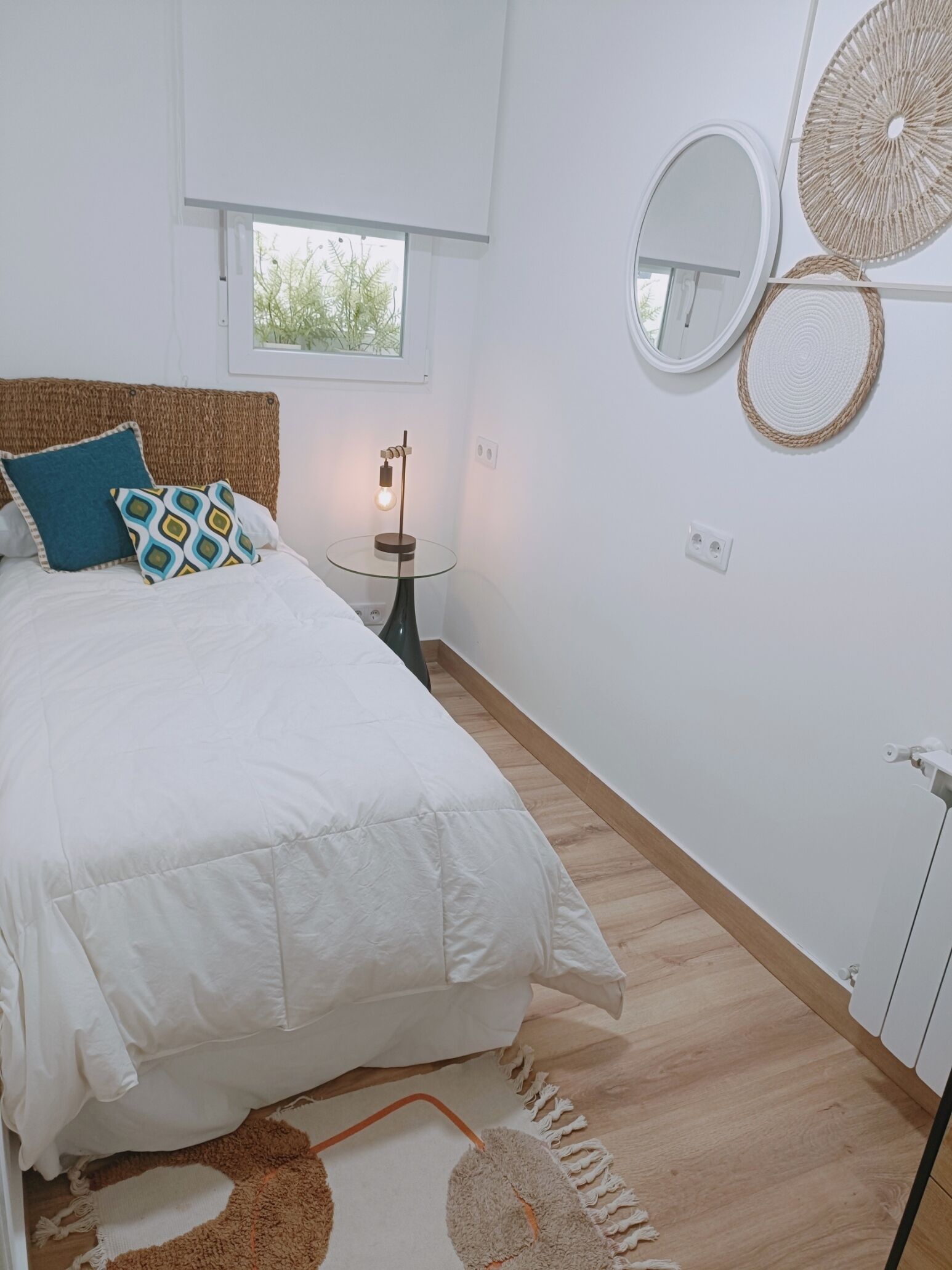 A bedroom with a bed, a bedside table with a lamp, a window, and wall decorations.