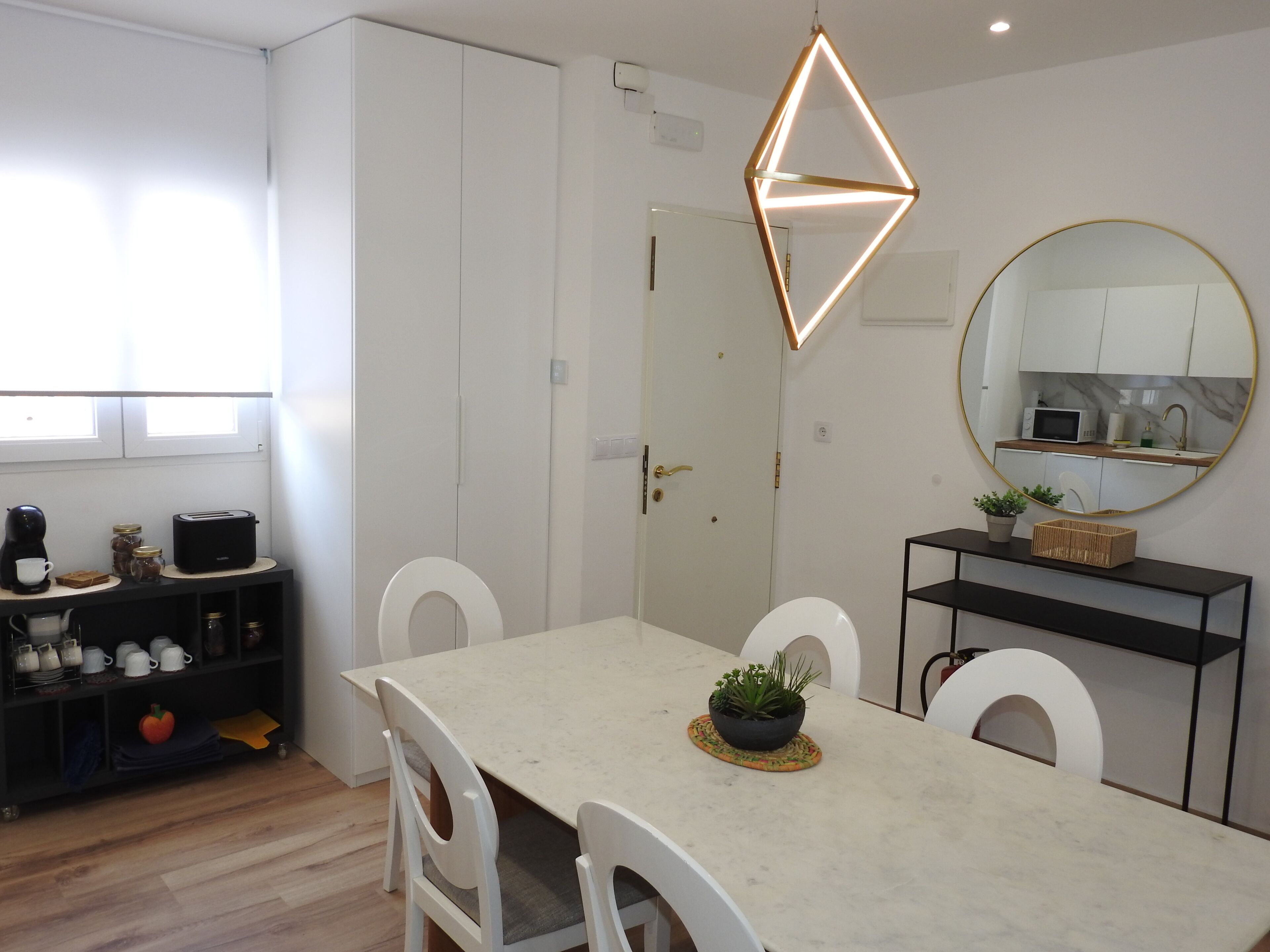 Une cuisine moderne avec un coin repas, des meubles blancs, un miroir rond et un luminaire au design géométrique.