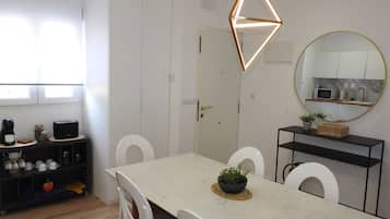 Une cuisine moderne avec un coin repas, des meubles blancs, un miroir rond et un luminaire au design géométrique.