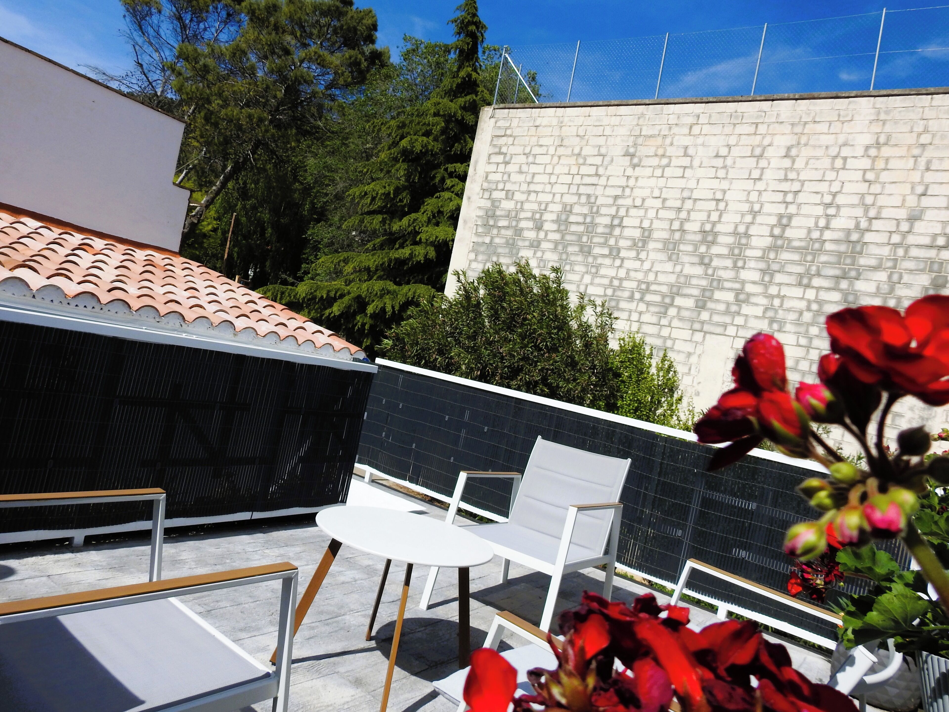 A rooftop terrace with a tiled roof, white chairs, and a brick wall.