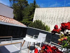 Una terraza en la azotea con techo de tejas, sillas blancas y un muro de ladrillo.