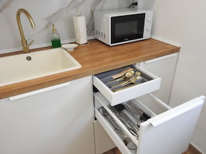 Una cocina con un lavamanos blanco, microondas y un cajón con utensilios.