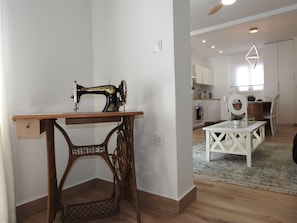 Una máquina de coser sobre una mesa de madera en una habitación con una cocina al fondo.