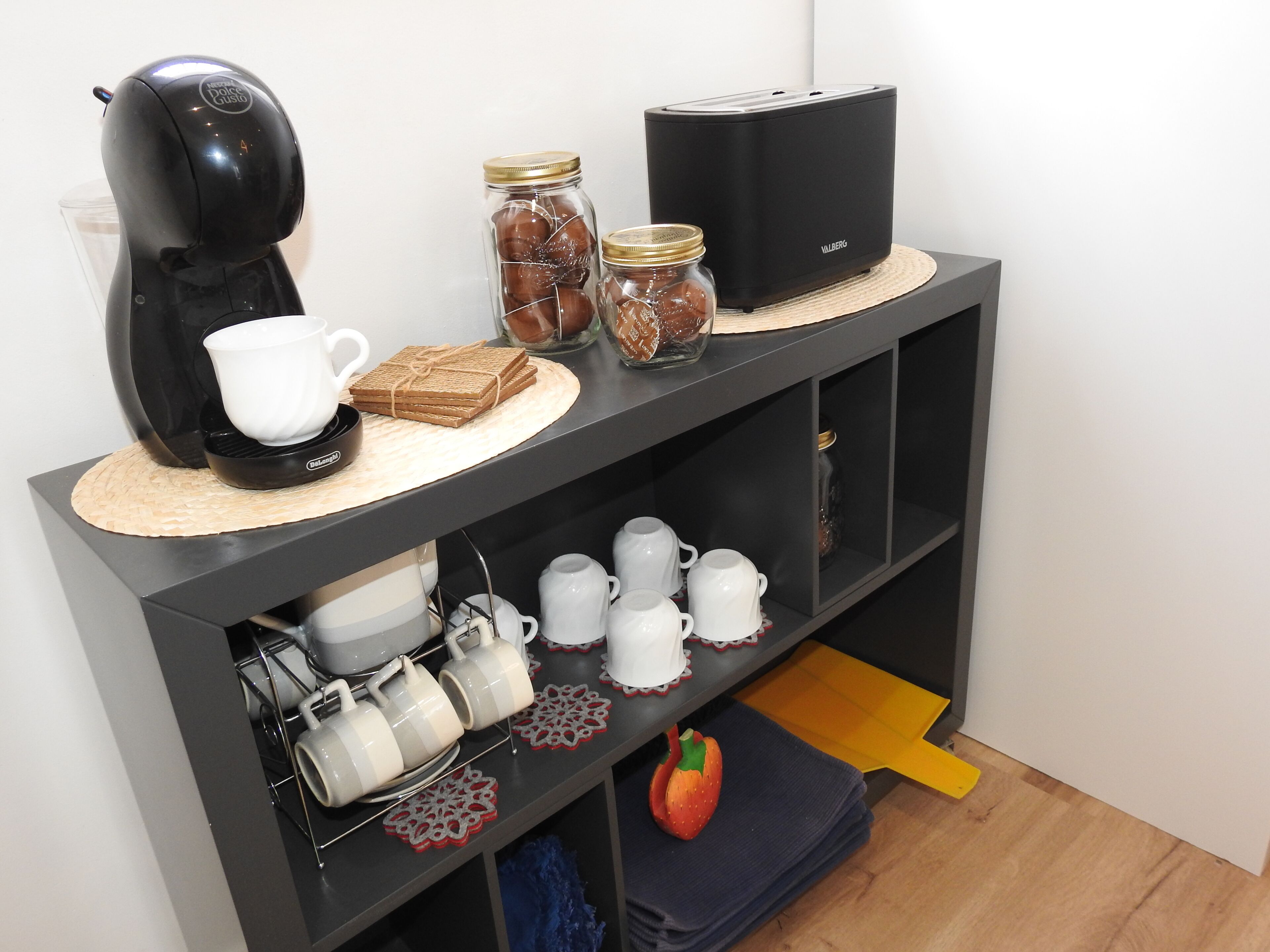 A kitchenette with a coffee maker, toaster, jars, and a toaster oven on a black countertop.