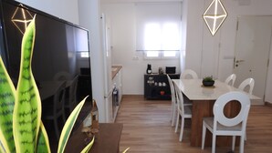 En moderne stue med et fladskærms-tv, et spisebord med stole, et tekøkken og en stor plante.