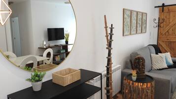 Una sala moderna con un espejo redondo, un adorno de madera, un sofá gris y un televisor sobre un mueble.
