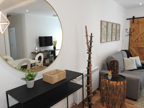 Ein modernes Wohnzimmer mit einem runden Spiegel, einer Holzdekorationssäule, einem grauen Sofa und einem Fernseher auf einem Schrank.