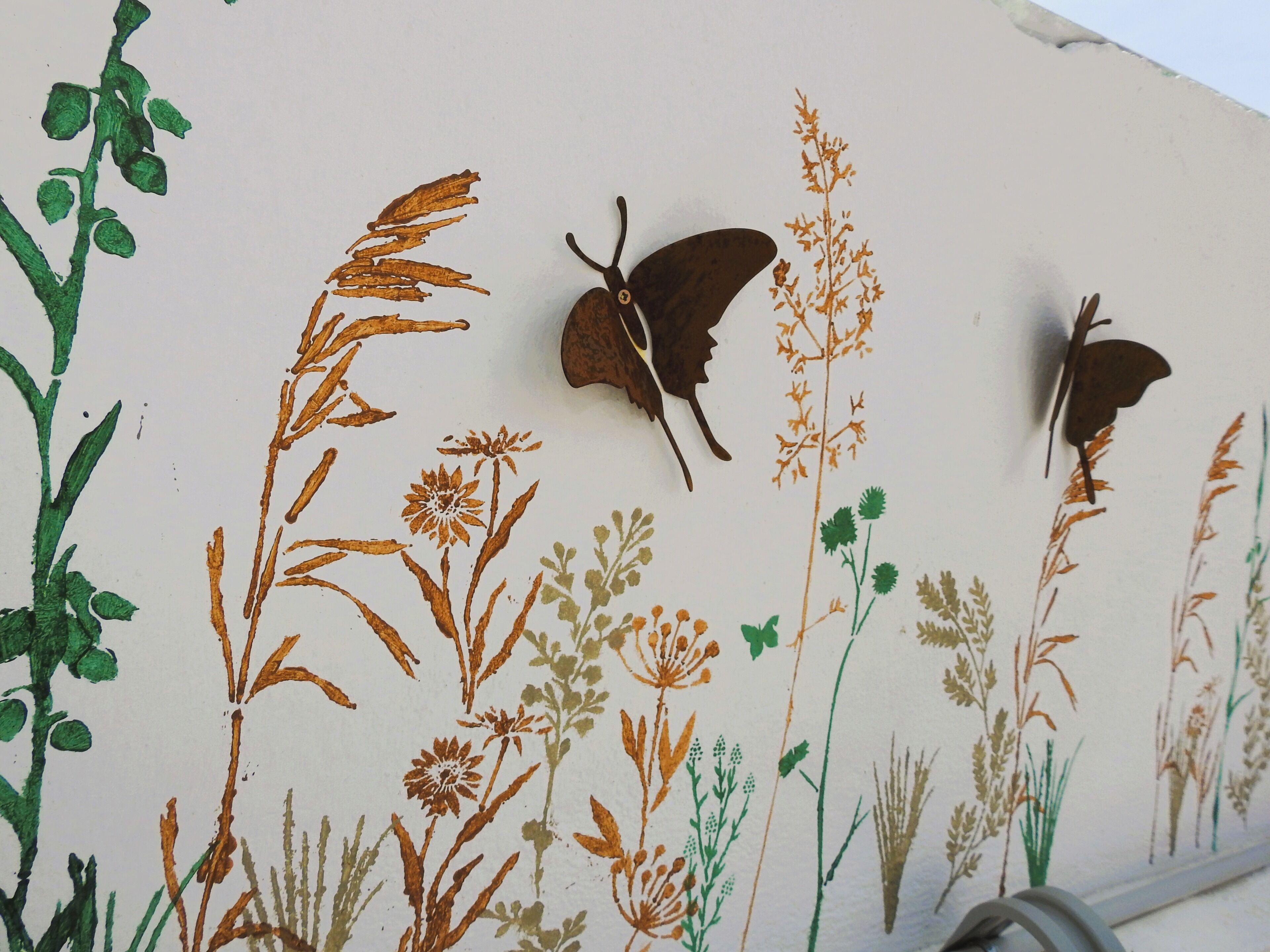 Een muur met een botanische muurschildering met verschillende planten en twee vlinders.