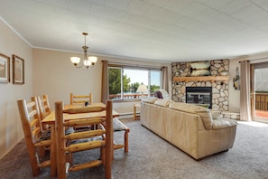 A living room with a stone fireplace, a dining table with wooden chairs, and a large window overlooking a lake. - Musky Point Lake House (Mercer)