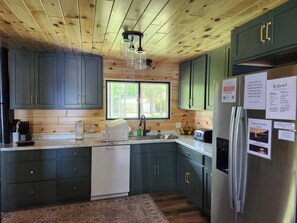 A kitchen with wooden ceiling, green cabinets, a white dishwasher, and a refrigerator with a note.