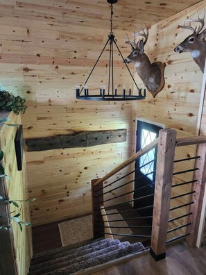 A wooden interior with a staircase, a chandelier, and deer antlers mounted on the wall.