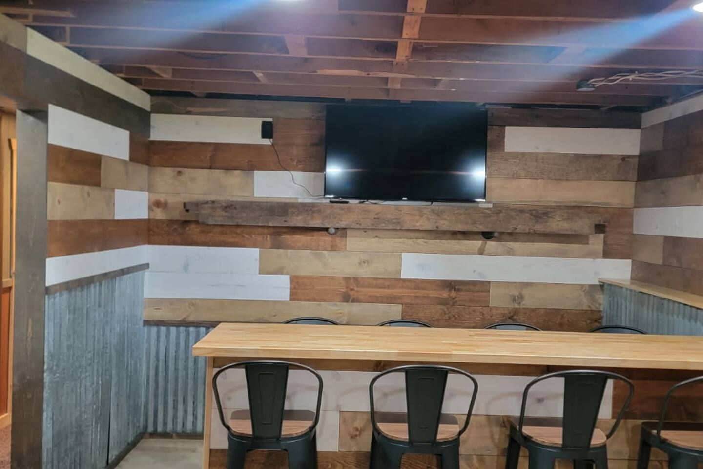 Ein Zimmer mit Wandverkleidung aus Holz, einem flachbildfernseher über einem Holztisch und vier Stühlen.