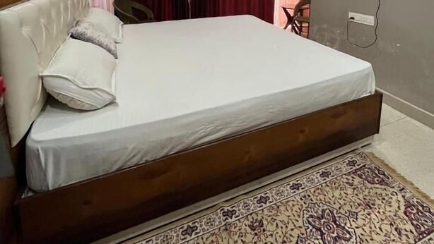 A bedroom with a bed, a ceiling fan, a TV mounted on the wall, and a patterned rug.