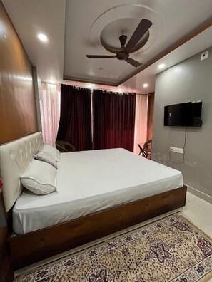 Un dormitorio con cama, ventilador de techo, televisor montado en la pared y alfombra estampada.