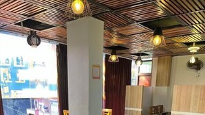 Een restaurant met houten tafels en stoelen, een hoog plafond met zichtbare balken en grote ramen die voor natuurlijk licht zorgen.