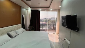 A bedroom with a bed, a ceiling fan, a television mounted on the wall, and a balcony with curtains.