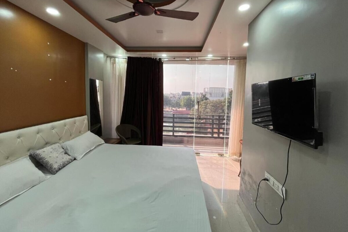 Ein Schlafzimmer mit einem Bett, einem Deckenventilator, einem an der Wand befestigten Fernseher und einem Balkon mit Vorhängen.