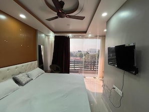 Un dormitorio con cama, ventilador de techo, televisor montado en la pared y un balcón con cortinas.