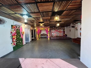 Un amplio salón con techo alto, un escenario con adornos florales y una zona de asientos.