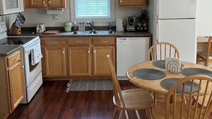 Una cucina con mobili in legno, un frigorifero bianco, un forno a microonde e un piano cottura. Si nota una finestra con persiane, un lavello e un tavolo da pranzo con sedie.