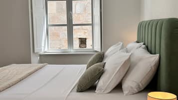 Quarto com cama, almofadas, abajur e janela com paredes de pedra.