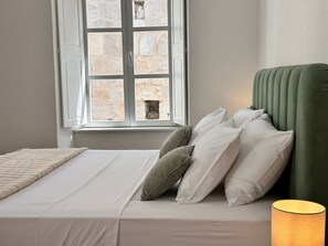 Quarto com cama, almofadas, abajur e janela com paredes de pedra.