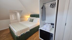 A bedroom with a bed, a wardrobe, and a small desk with towels.