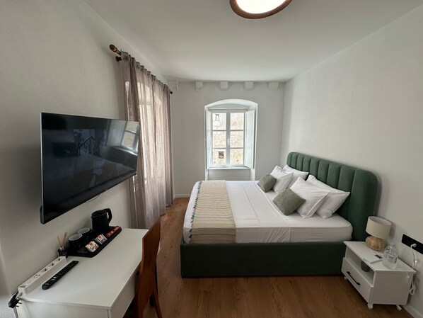 A bedroom with a bed, a TV, a desk, and a window.