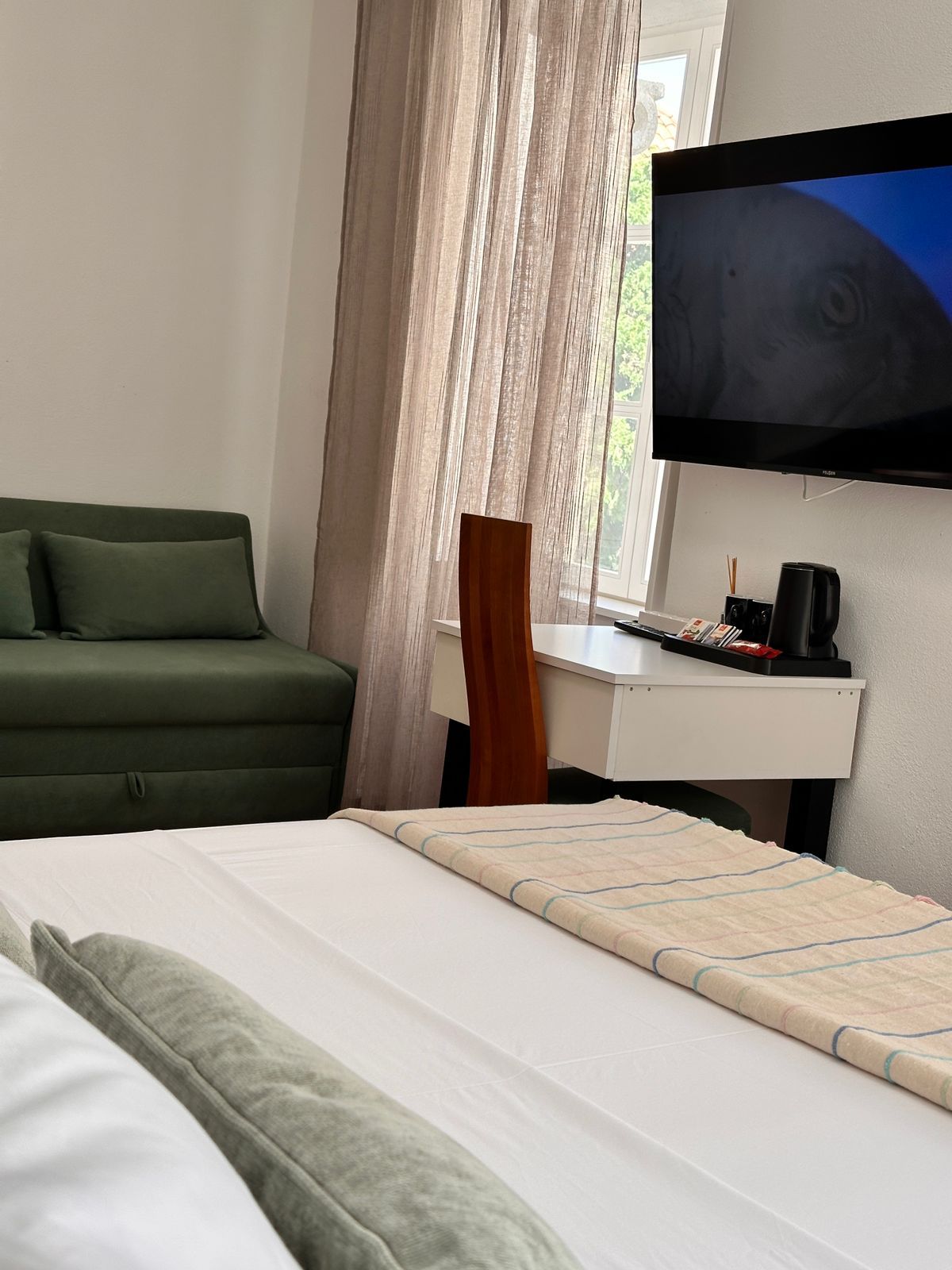 Una habitación de hotel con cama, escritorio, televisor y ventana con cortinas.