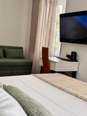 Una habitación de hotel con cama, escritorio, televisor y ventana con cortinas.