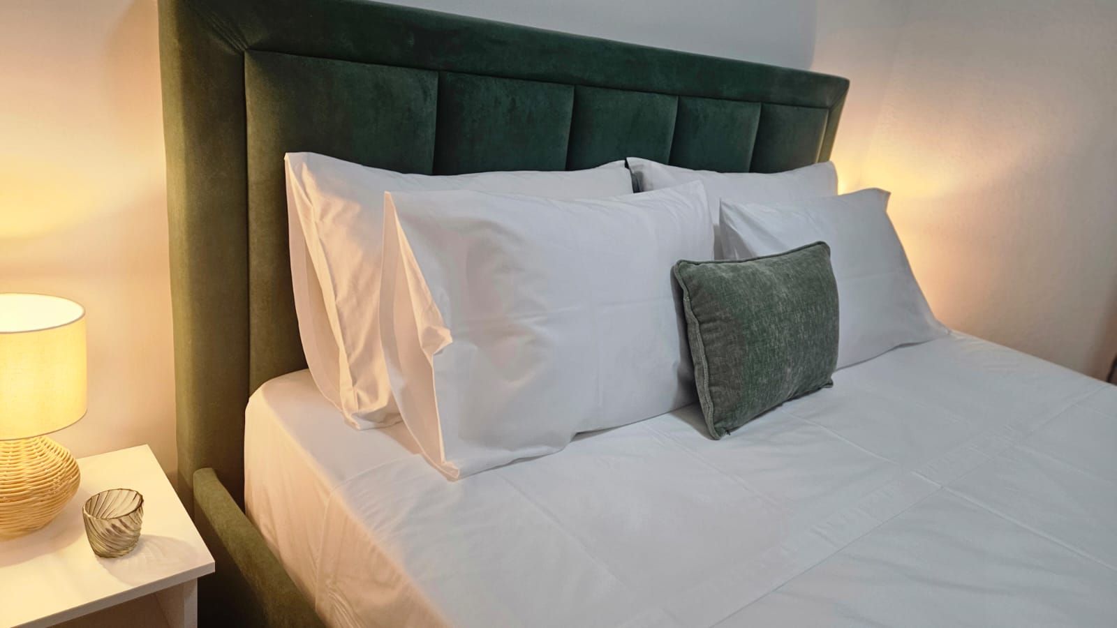 Una cama bien hecha con ropa blanca y un cabecero tapizado en verde.