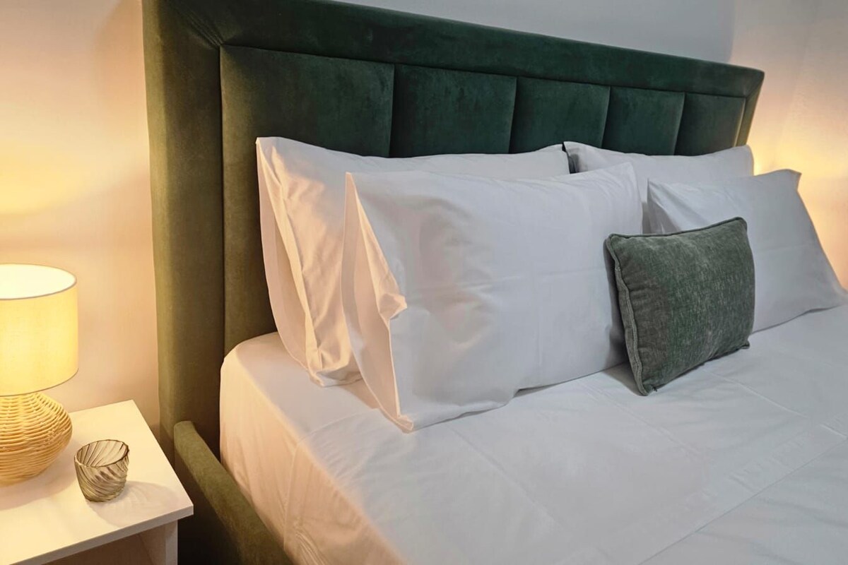 Cama bem arrumada com roupa de cama branca e cabeceira estofada em verde.