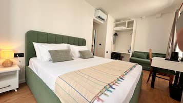 Quarto de hotel com cama, mesa de cabeceira, abajur, guarda-roupa e secretária com cadeira.
