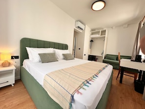 Habitación de hotel con cama, mesita de noche, lámpara, armario y escritorio con silla.