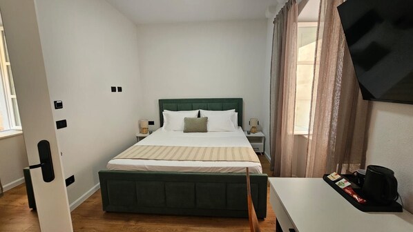 A hotel room with a bed, bedside tables, a desk, and a window with curtains.