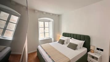 Quarto com cama, mesa de cabeceira, abajur e janela.