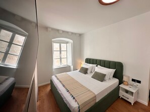 Quarto com cama, mesa de cabeceira, abajur e janela.
