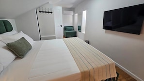 Quarto de hotel com cama, uma cadeira verde, televisão e porta com cabideiro.