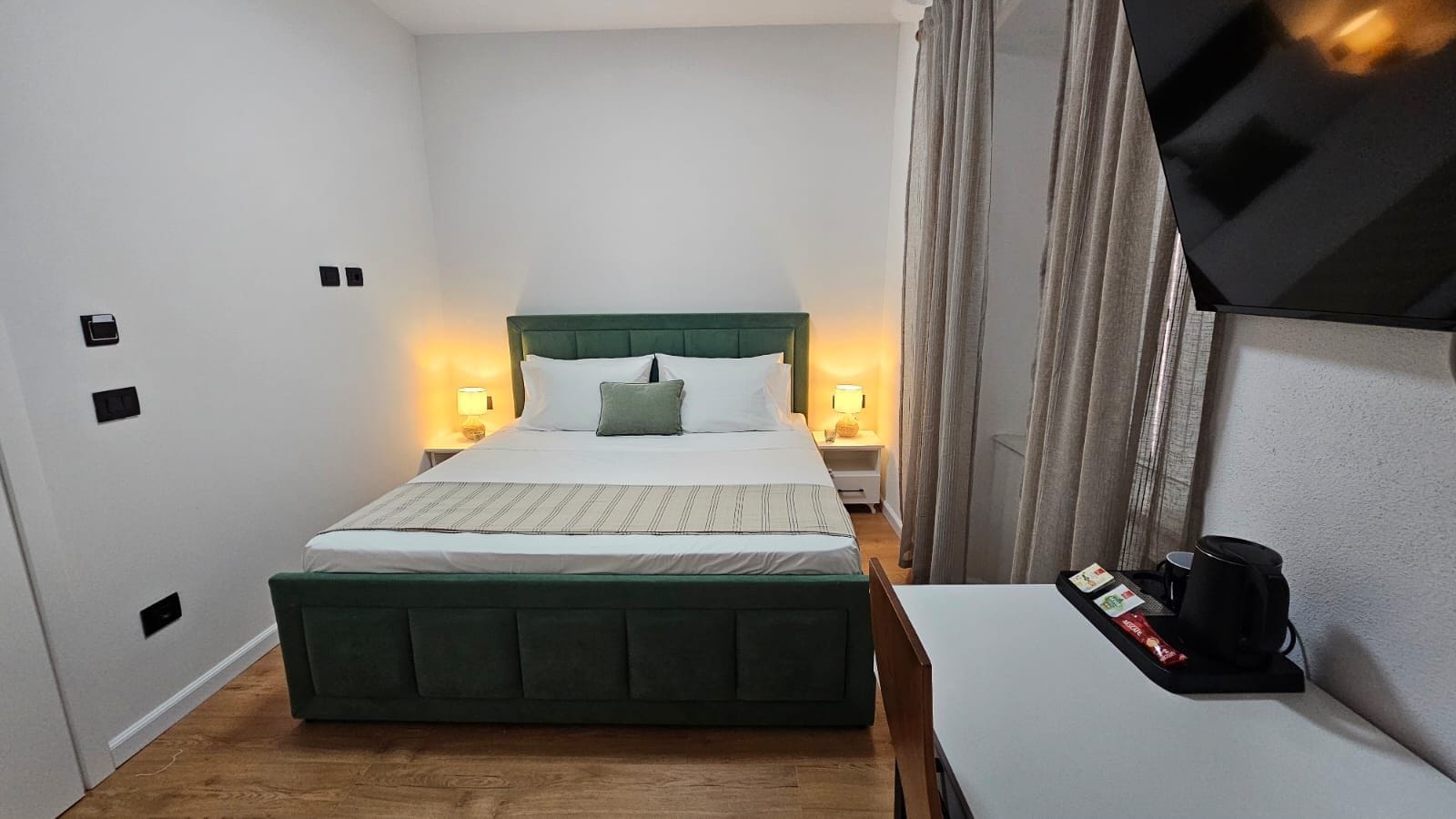 Una habitación de hotel con una cama, mesitas de noche, un escritorio y un televisor.