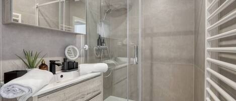 Un baño moderno con cabina de ducha de vidrio, tocador con espejo y perchero para toallas.