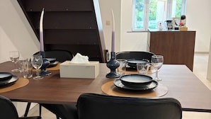 Uma sala de jantar moderna com mesa de madeira posta para quatro, cadeiras pretas e uma escada ao fundo.