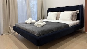 Um quarto moderno com uma cama azul escura, almofadas brancas e um edredom cinzento.