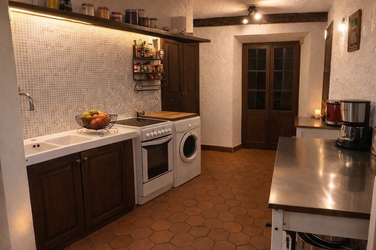 Una cocina con salpicadero de azulejos, armarios de madera, un lavabo, una estufa, una lavadora y una encimera con una cafetera.