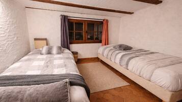 A room with two beds, a window with curtains, a wooden ceiling, and a tiled floor.
