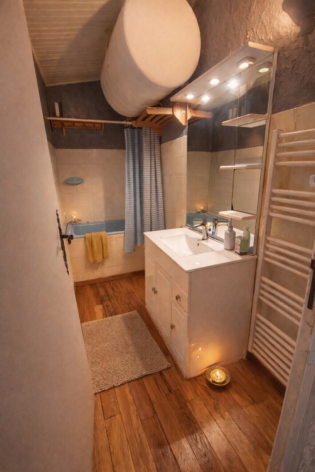 Un baño con suelo de madera, un lavamanos blanco, un espejo y un perchero para toallas.